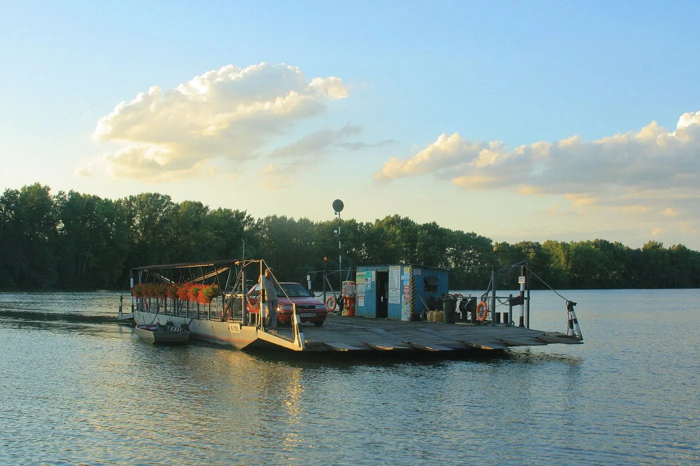 Kisebb komp autóval a Tisza vizén, háttérben ártéri erdő, naplementében