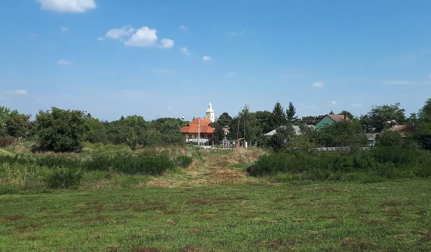 Falusi látkép a gátról: rét, fák és egy fehér tornyú templom